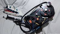 Proton pack with attached gun and Ecto-1 car replica showing detailed wiring and vintage design, photographed on white background.
