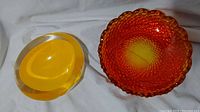 Two ashtrays placed side by side showing colors and shapes, one orange hobnail glass, one yellow crystal with clear edges