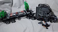 Black LEGO Technic semi truck with attached trailer featuring green crane machinery on a fabric surface.
