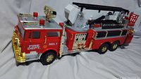 Side view of vintage large red firetruck collector's toy showing detailed moldings, lights, ladders, and wheels.