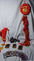 Full view of lot showing Chinese hanging firecrackers, coins, red envelopes, small figurines, and Yu-Gi-Oh! cards displayed.