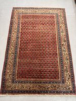Full view of rectangular red field rug with border and fringe