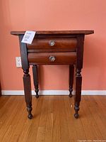 Front view of antique side table showing two drawers with metal pull handles and turned legs.