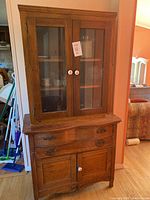 Front view of antique wooden cabinet showing glass front doors on upper section with interior shelves and drawers below.