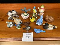 Full view of all 12 assorted bird figurines on wooden surface showing various sizes, colors, and styles.