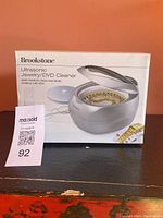 Box of Brookstone Ultrasonic Jewelry/DVD Cleaner showing brand and product image.