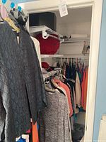Photo showing hanging clothes in a bedroom closet including sweaters, tops, dresses, and jackets in multiple colors and styles