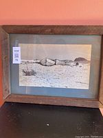 Framed black and white photograph showing three wooden beach boats in sand, matted and framed in a rustic wood frame with visible grain and weathering.