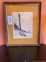Frontal view of the framed black and white sketch art showing the lighthouse, rowboat and ship with some wear on the frame edges.