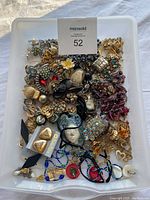 Top view of assorted jewelry pieces in a white container showing necklaces, earrings, brooches, and pendants with various colors and materials.