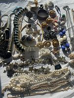Overview of assorted jewelry including necklaces, bracelets, earrings, and brooches laid flat on white fabric with natural lighting