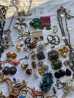 Photo showing a variety of jewelry including necklaces, earrings, bracelets, brooches, and rings arranged on a light surface.