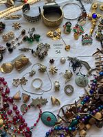 Top down view of assorted jewelry items spread on a flat surface including necklaces, earrings, brooches, bracelets, and rings, showing variety of styles and materials.