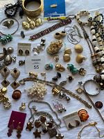 Top-down view of assorted costume jewelry pieces laid out on white cloth including multiple necklaces, earrings, bracelets, and brooches.
