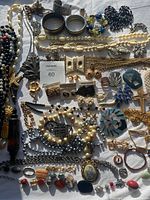 Top-down view of assorted jewelry including necklaces, earrings, brooches, rings, and bracelets laid out on a white cloth, showing wide variety of colors and styles.