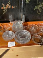 Photo of the large assortment of Candlewick glass items arranged on wooden surface, showing plates, glasses, candlestick holders, and divided dishes with characteristic beaded detail.