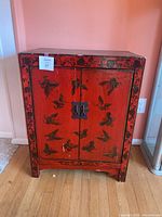 Front view of the red painted wooden cabinet with black bird motifs and metal latch on the doors