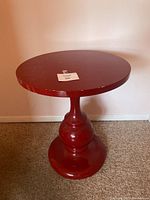 Side view of red lacquer side table showing round top and pedestal base.