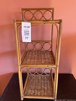 Front view of the small wicker bookshelf showing three woven shelves and circular loop decorative back supports.