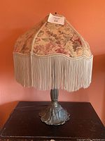 Full view of table lamp showing floral fabric lampshade with fringe and metal base