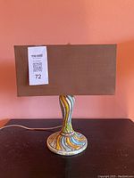 Full view of the table lamp showing the brown rectangular lampshade and the colorful ceramic base with wavy patterns in multiple colors.