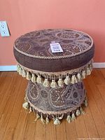 Side angle view showing the tassel trim around the middle and base, patterned fabric, and padded top.