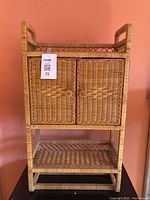 Front view of vintage wicker cabinet showing two woven doors and lower open shelf.