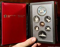 Full view of open black presentation box with red satin interior and seven proof coins in clear display holder.