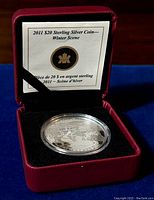 Front view of 2011 $20 Sterling Silver Coin showing the winter scene with horses and trees, encased in plastic, displayed in red presentation box.