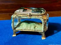 Front and side view of small antique jewelry casket showing brass frame, beveled glass panels, and cushioned green silk interior