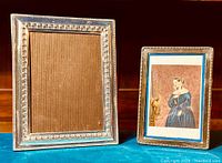 Two antique silverplated picture frames side by side, one larger and one smaller with different inserts inside.