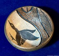 Top view of the round pottery bowl with a black bird motif in flight and textured sgraffito decoration on the opposing side.