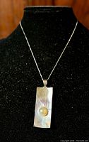 Front view of rectangular sterling silver pendant with centrally inset large round Mabe pearl on black jewelry display bust, showing iridescence on pendant surface and attached silver chain.