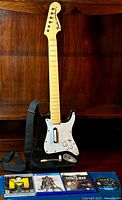 Rock Band guitar controller with strap and four PlayStation game cases laid out on a wooden surface.