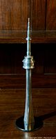Full frontal view of the aluminum CN Tower sculpture with lucite base, placed on a wooden surface against a dark wood background.