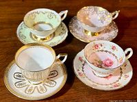 Four fine bone china vintage teacups each paired with matching saucers shown on a wooden surface in varying pastel and gold floral designs.