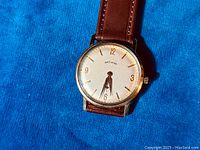 Front view of watch dial and leather strap on blue background