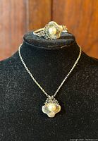 Close-up of bracelet and pendant on black display with pearl center and detailed silver fan-like design.