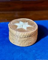 Close-up of the woven basket with porcupine quill star decoration on lid, displayed on blue cloth.