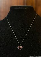 Front view of the bird-shaped Bohemian garnet pendant on the silver chain displayed on a black necklace stand.