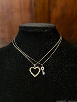 Front close-up of both rhinestone pendants displayed on black velvet jewelry bust. Shows heart and key pendants and sterling chains clearly.