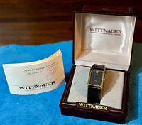 Wittnauer tank style wristwatch inside its original Wittnauer box with owner information booklet to the side, displayed on blue fabric.