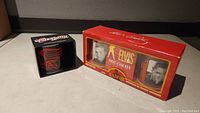 Two boxed mug sets, one red Elvis Presley hot cocoa 2-mug box and one black Aerosmith mug box.
