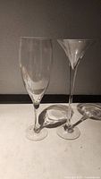Pair of oversized glasses showing large wine glass and large martini glass side by side on a plain surface with shadows.