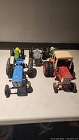 Front view of 5 diecast tractors arranged in two rows on a white surface showing different colors and models including green John Deere, blue Ford, red International Harvester, and a red homemade model.