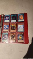Image showing nine Yu-Gi-Oh cards inside a red binder sleeve with a mix of monster and spell cards in good condition.