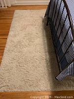 Off-white rectangular shag rug alongside a metal-framed bed on hardwood floor.
