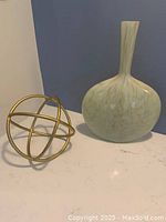 Large opal green glass vase next to brass decorative sphere on white surface with blue-gray background.