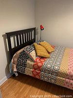 View of the bed frame assembled with colorful bedding and pillows showing the front and side profile including headboard and footboard.