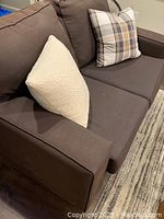 Brown two-seater Ikea KIVIK sofa showing left armrest, cushions, two accent pillows on seat.
